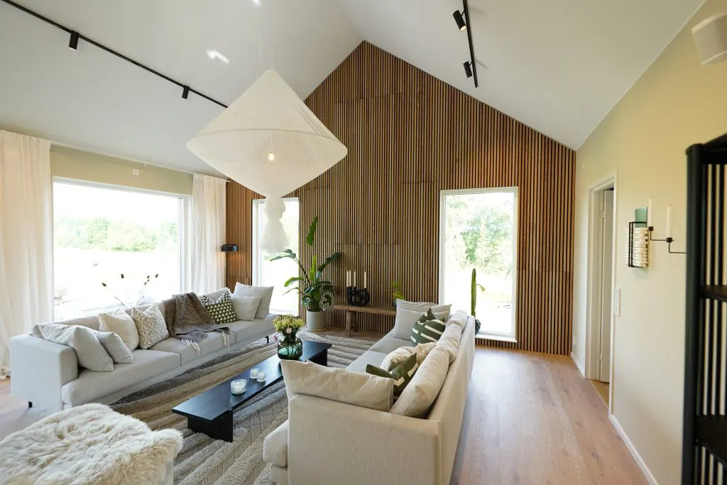 Salon moderne avec un haut plafond, de grandes fenêtres, des canapés légers, un mur daccent en bois acoustique Akupanel, des plantes dintérieur et une lumière naturelle abondante.
